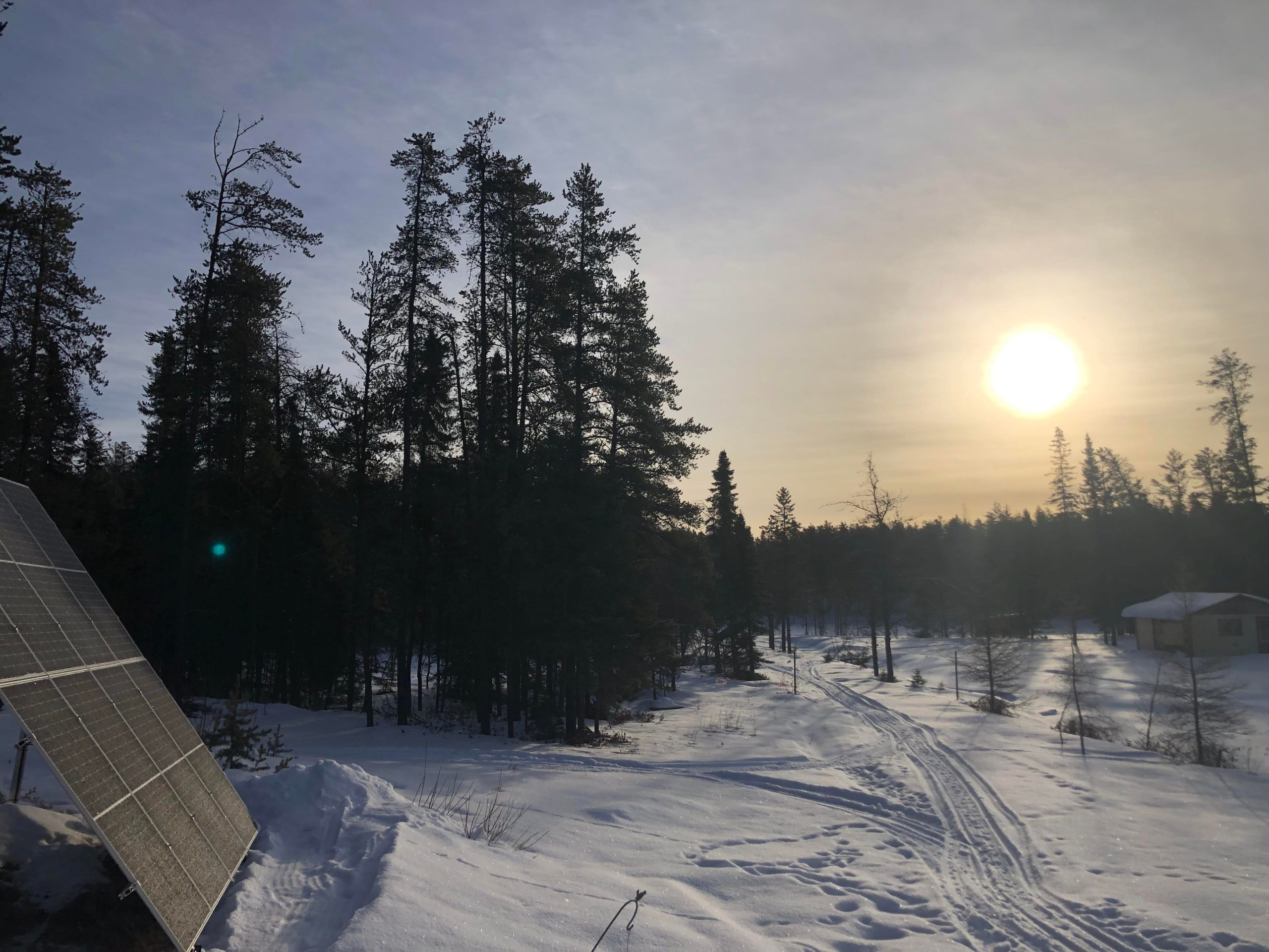Un soleil de plomb rayonne dans un ciel d'hiver. Une forêt de l'Abitibi-Témiscamingue entour des panneaux solaires. 